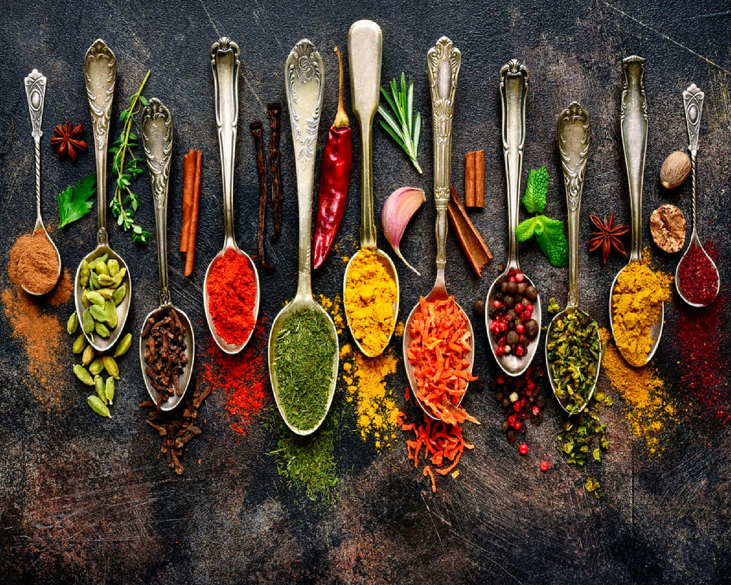 Assortment of natural spices on vintage spoons on dark slate